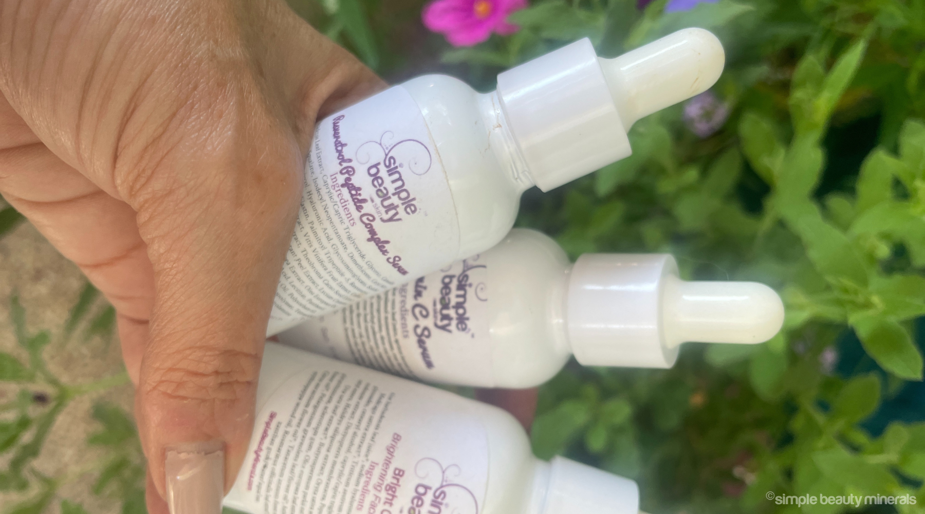 hand holding white dropper bottles of facial serums.