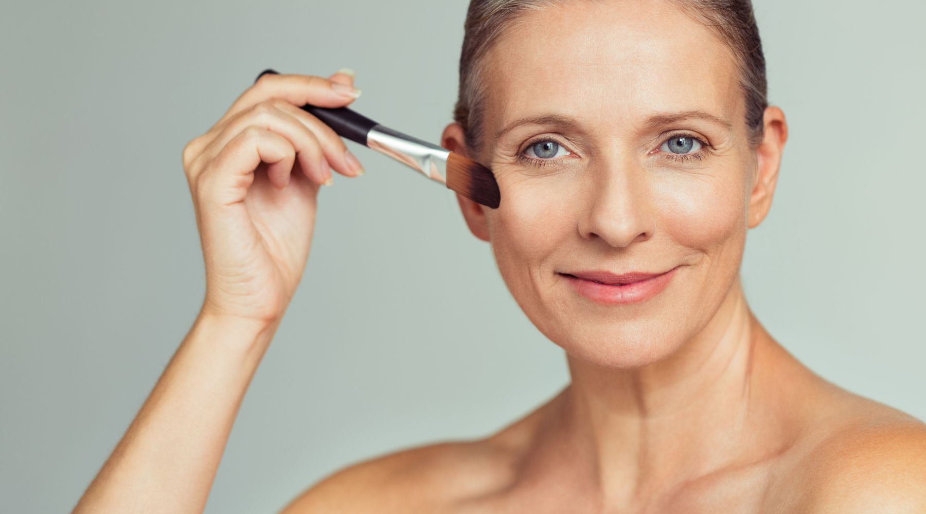 mature woman applying blush with makeup brush.