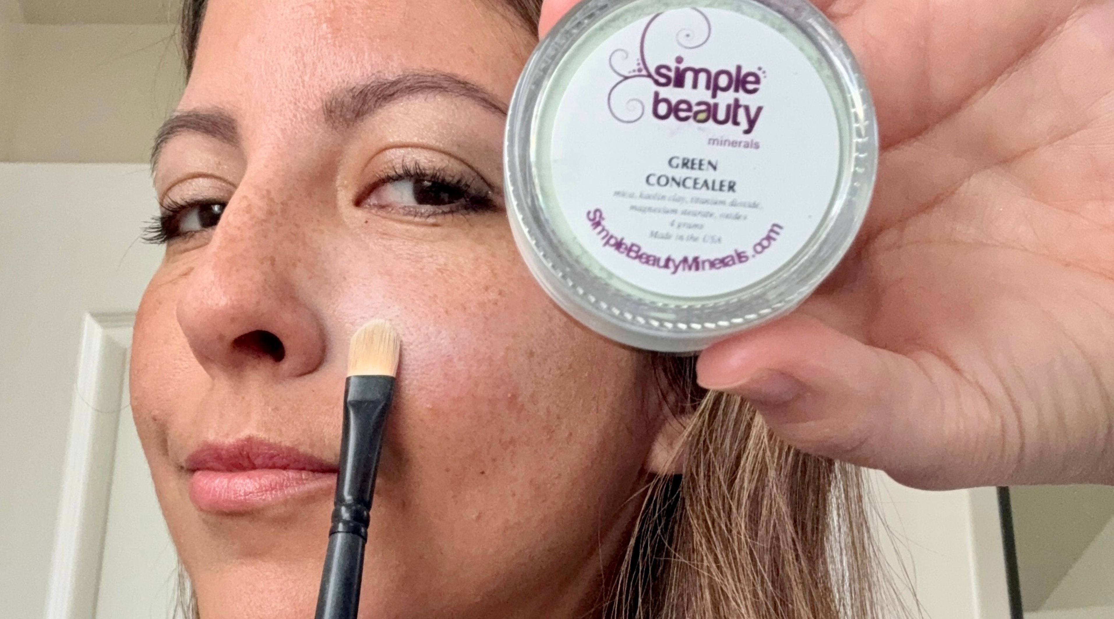 mature woman with concealer brush and concealer in hand.