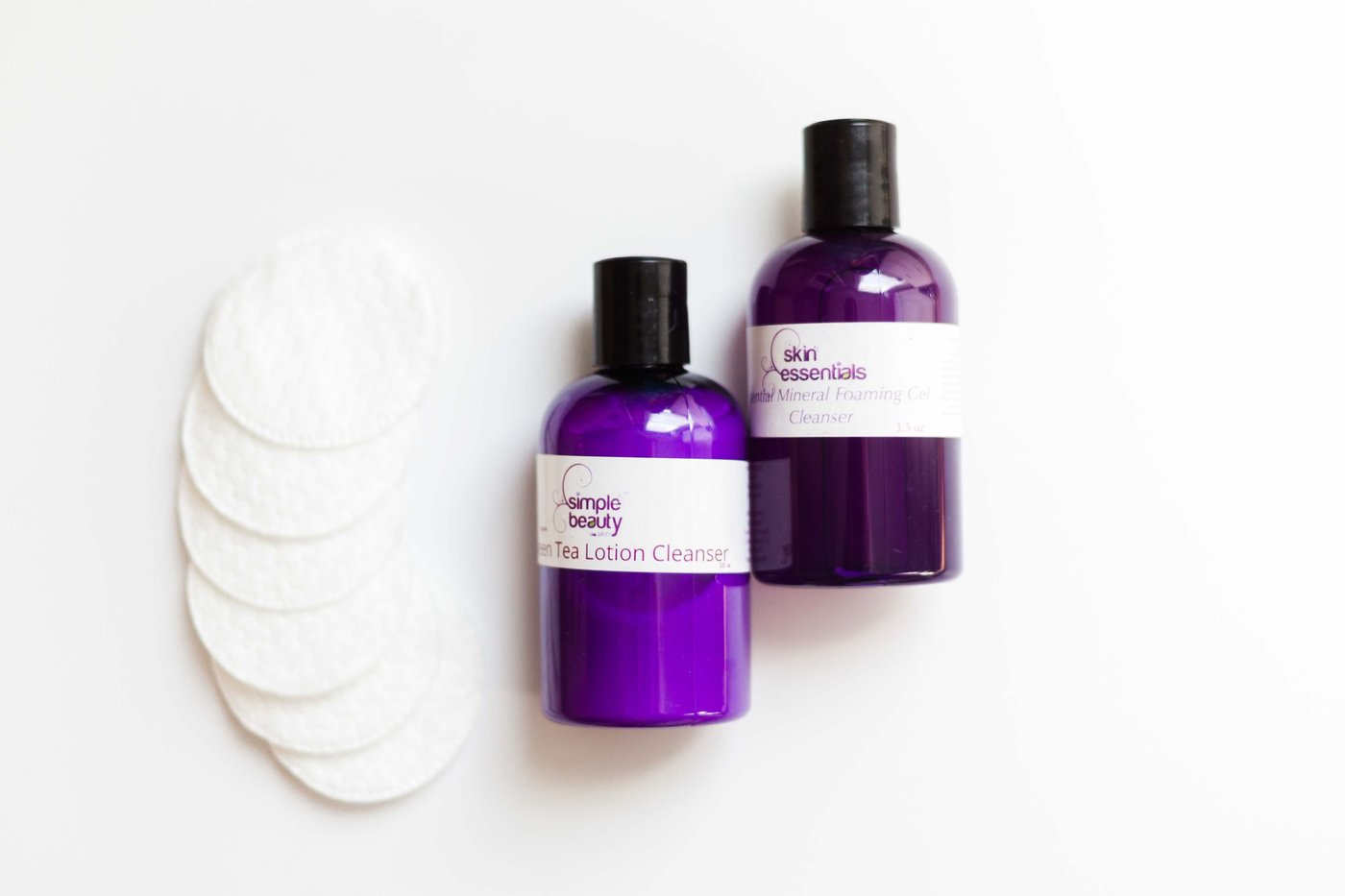 two cleansers in purple bottles with cotton pads next to them