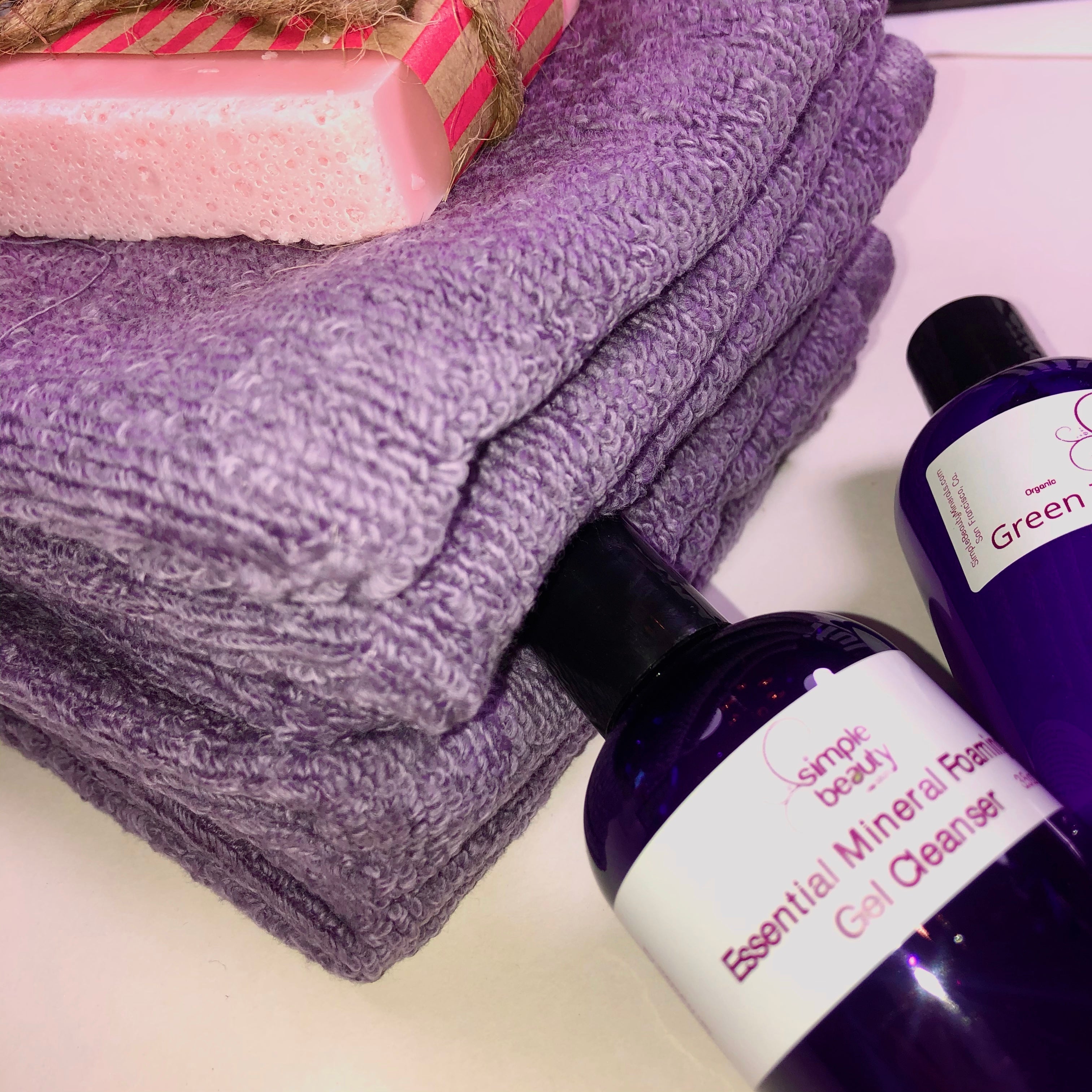 stack of purple wash clothes with pink bar and cleansers