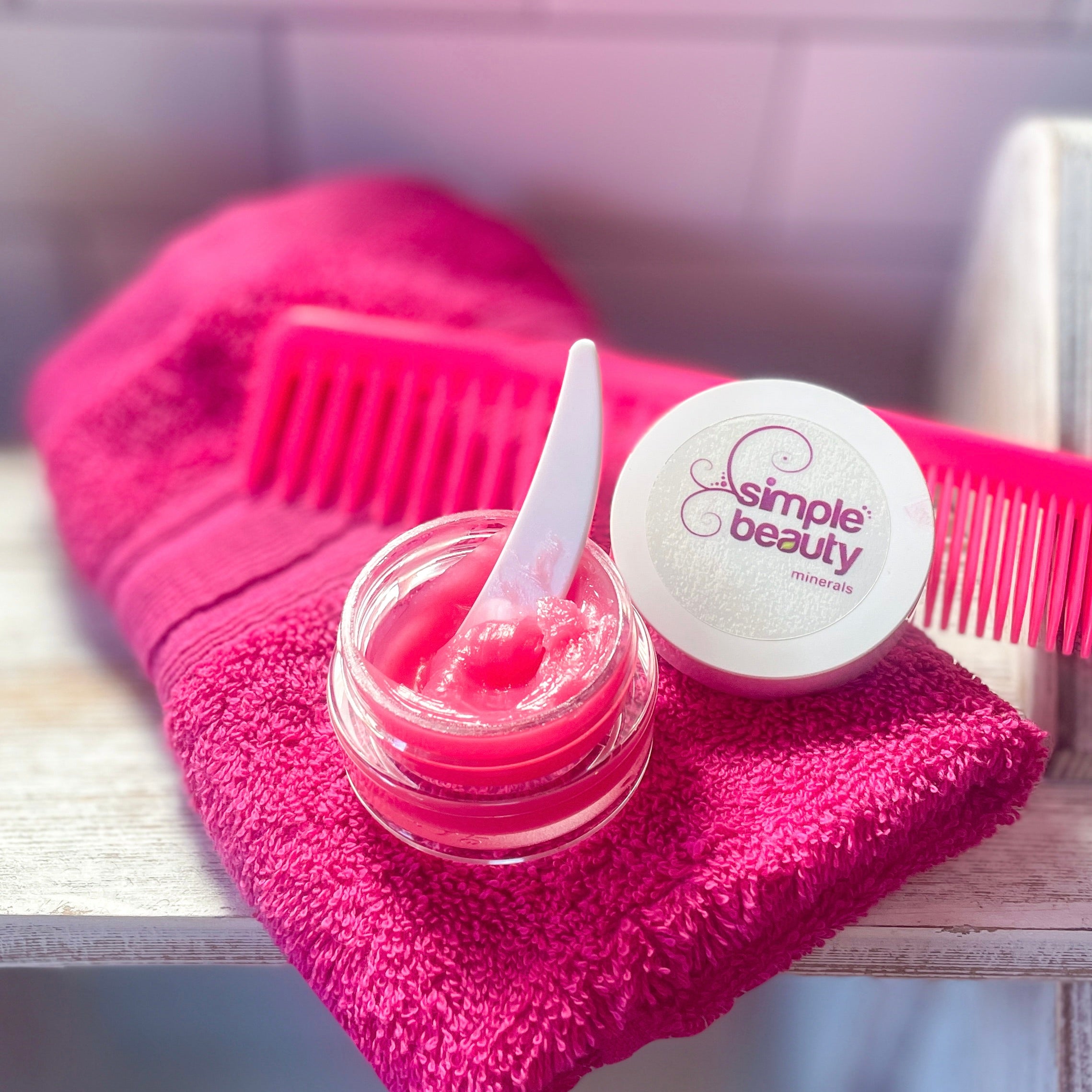 lip sleeping mask open with spatula, pink comb and pink washcloth.