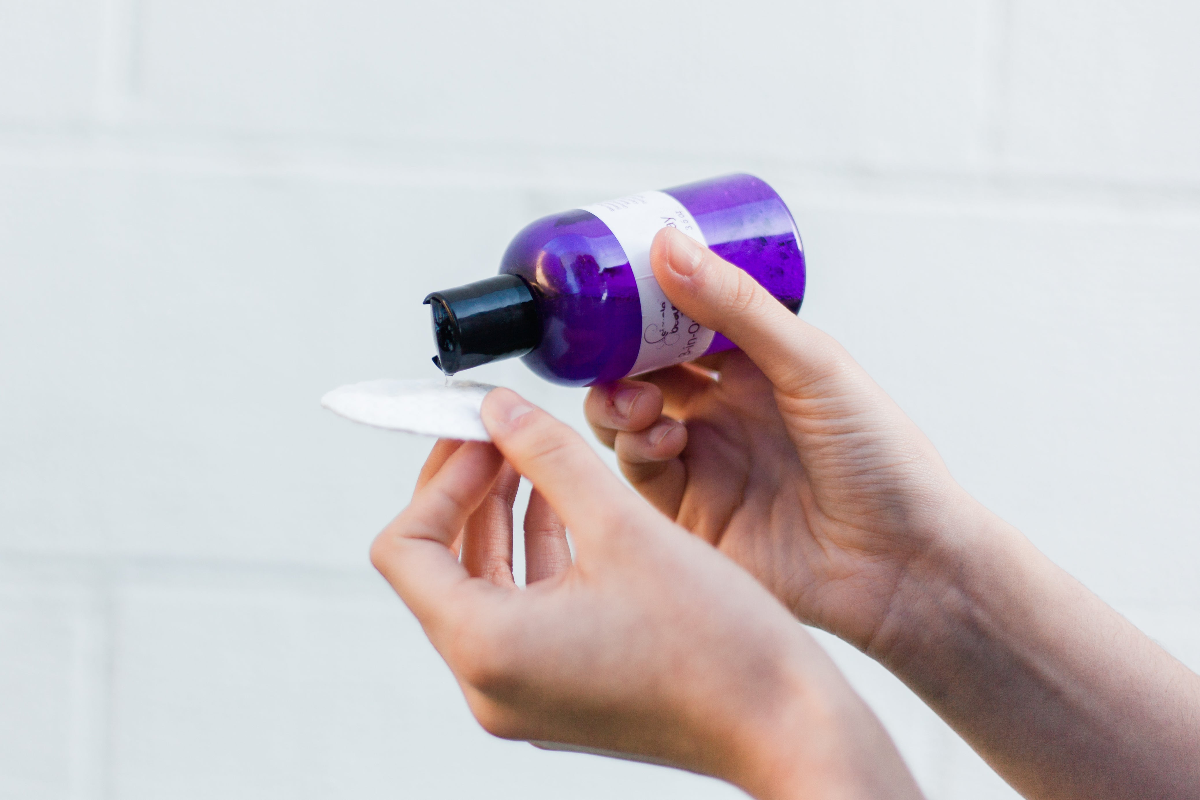 cleanser in purple bottle pouring onto cotton round