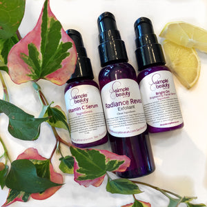 3 purple skin care bottles, 2 serums and a leave on exfoliant nestled with greenery and lemon