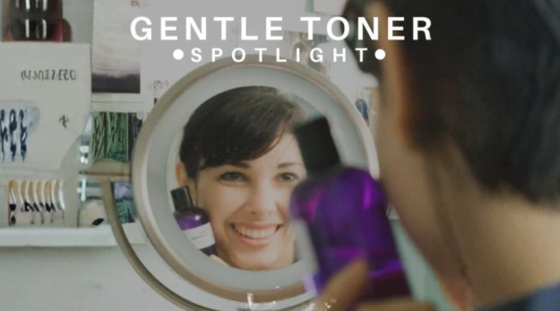 reflection of a smiling woman holding a purple bottle of skincare product.