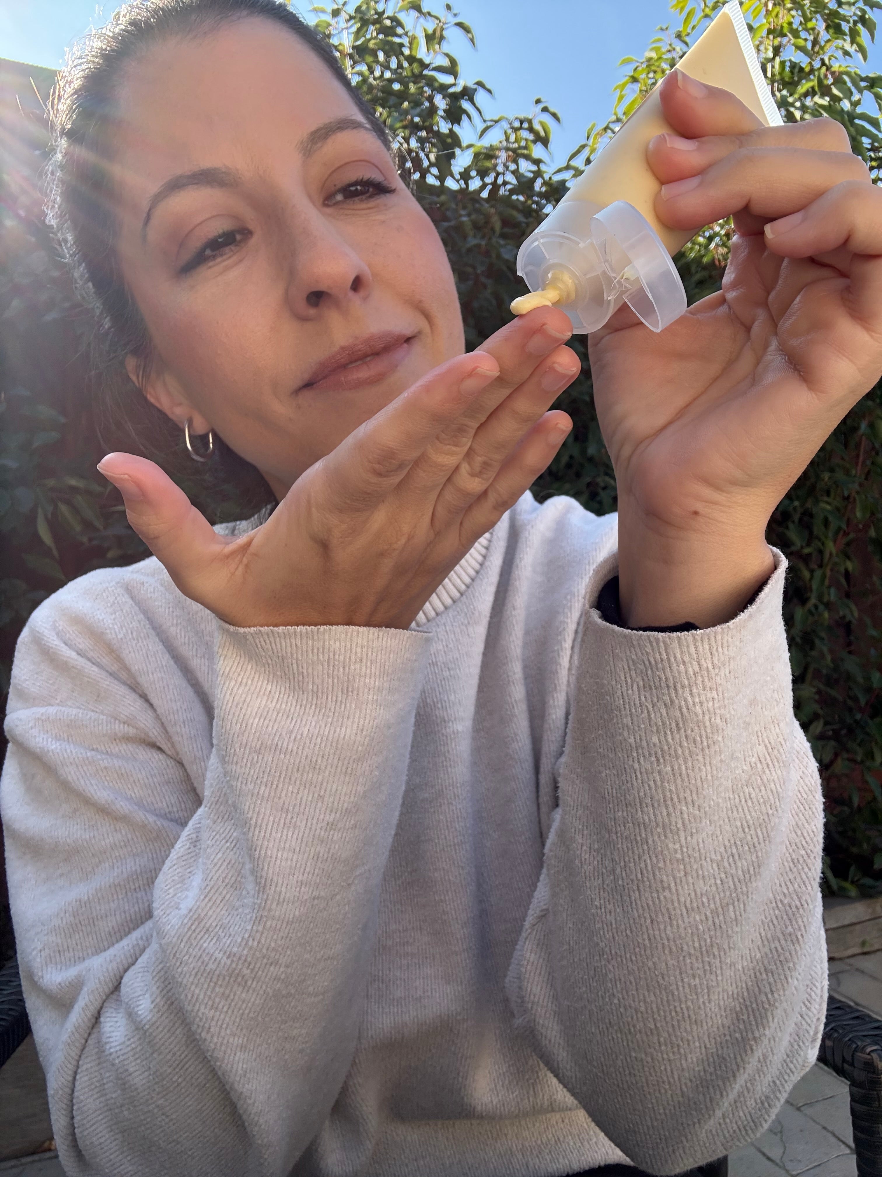 woman holding a lotion tube outdoors with greenery in the background.
