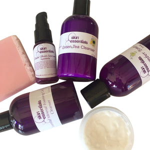 group of cleansers in purple bottles with pink soap and open jar of creme